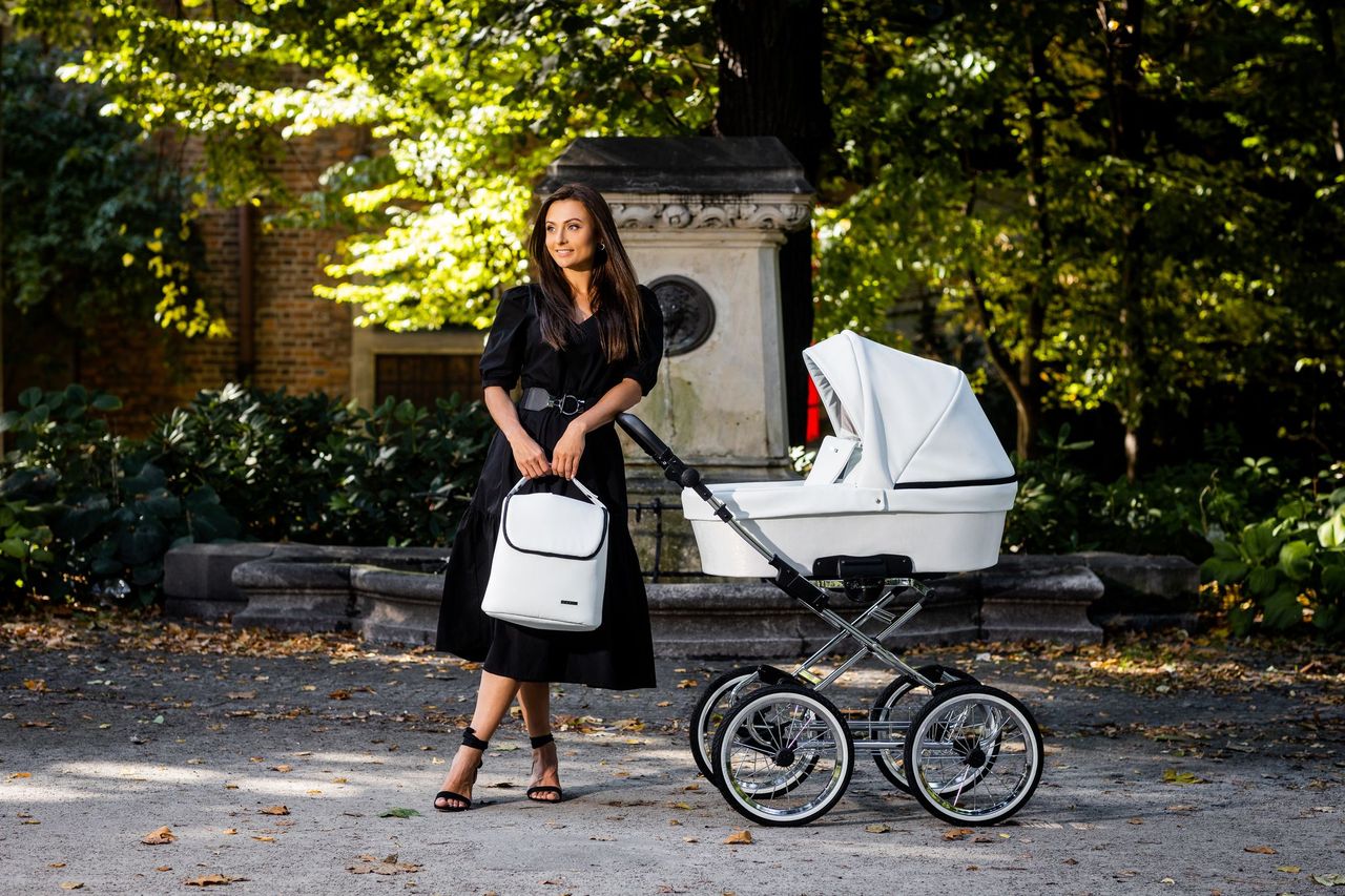 Kobieta w czarnej sukience obok wózka retro Romantic Kunert z dużymi kołami w parku.